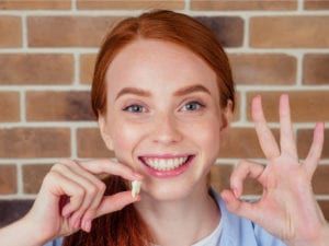 A patient holding an extracted tooth and smiling while flashing OK sign
