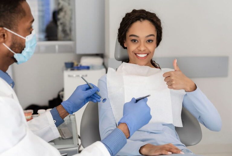 Satisfied black woman showing thumbs up in modern dentist cabinet, doctor holding dentist tools