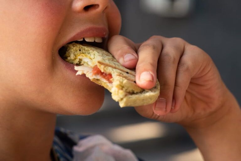 Teenage boy eating snacks close-up. Snack, sweets, street food. Intermediate meal. Mouth with teeth, tongue and saliva macro shot.